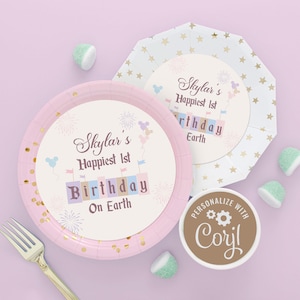 以下が含まれることがあります： ゴールドのグリッターのアクセントと「Skylar's Happiest 1st Birthday On Earth」と書かれたパーソナライズされたデザインが施されたピンクと白の紙皿。皿は花火、風船、城で飾られています。デザインには「Corylでパーソナライズ」というテキストも含まれています。