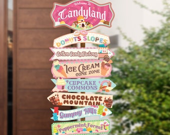 Pode incluir: Um poste indicador de madeira com várias placas direcionais que apontam para diferentes áreas de uma festa temática do Candyland. As placas são decoradas com doces e guloseimas coloridos. A placa superior diz "Bem-vindo ao Candyland".