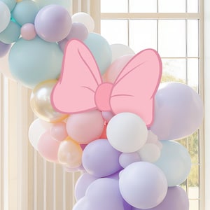 Puede incluir: Un arco de globos hecho de globos de colores pastel con un gran lazo rosa en la parte superior.