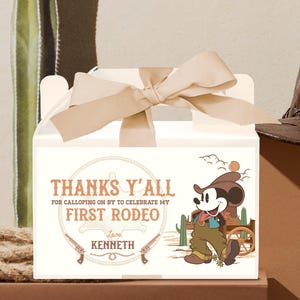 May include: White favor box with a brown ribbon and a Mickey Mouse character dressed as a cowboy. The box has the text "Thanks Y'all for Galloping On By to Celebrate My First Rodeo Love, Kenneth".