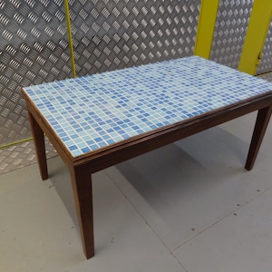 May include: A rectangular coffee table with a mosaic tile top in shades of blue and white. The table has a dark brown wooden frame and legs. The table is approximately 122 cm long, 61 cm wide, and 46 cm high.