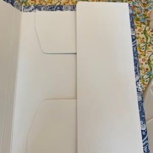 May include: An open white file folder with two pockets and a blue paisley border. The folder is on a floral patterned surface. The folder is designed to hold documents and papers.