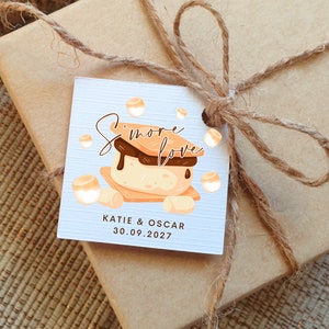 May include: A white tag with a brown and orange illustration of a s'more. The text "S'more Love" is written in brown cursive. The tag also includes the text "KATIE & OSCAR 30.09.2027".