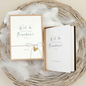 Könnte beinhalten: Zwei weiße Karten mit goldenen Akzenten und schwarzem Text, der "Weil du etwas ganz Besonderes bist" mit einem kleinen goldenen Herzen lautet. Die Karte links hat das Wort "Marlene" unter dem Text. Die Karte rechts hat die Worte "Lieblingsmensch" unter dem Text. Beide Karten befinden sich in braunen Pappkartons.