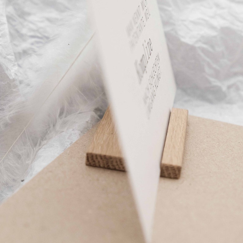 Puede incluir: Una tarjeta blanca con texto est&aacute; apoyada por dos bloques de madera. La tarjeta est&aacute; sobre una superficie marr&oacute;n.