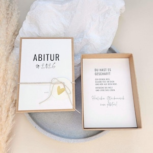 Könnte beinhalten: Eine Geschenkbox zur Graduierung mit einer weißen Karte mit der Aufschrift "ABITUR #2026" in schwarzer Schrift. Die Karte ist mit Bindfaden und einem goldenen Herzaufkleber gebunden. Die Box enthält eine Karte mit deutschem Text.