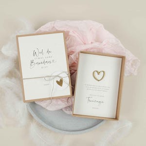 Op de afbeelding: Twee kleine geschenkdozen met een lichtbruine achtergrond. De bovenste doos heeft een witte kaart met de tekst "Weil du etwas ganz Besonderes bist" en een klein gouden hart. De onderste doos heeft een witte kaart met de tekst "Ich wünsche dir die  welt bester, dich an meiner Seite zu haben.  Denn an dir hab ich  braucht  mehr.  Wichtiger  du meine  Tranzenzen  werden." en een gouden hart.