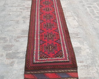 May include: A long, red runner rug with a geometric pattern in shades of blue, black, and white. The rug has fringe on both ends.