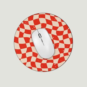 May include: A white wireless computer mouse sits on a round mousepad. The mousepad has a red and cream checkered pattern with a distressed, vintage appearance. The mouse is in the centre of the pad, ready for use.