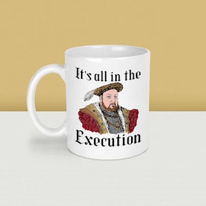 May include: White ceramic mug featuring a portrait of a historical figure with a feathered hat and ornate clothing. The mug has the text "It's all in the Execution" in black lettering.