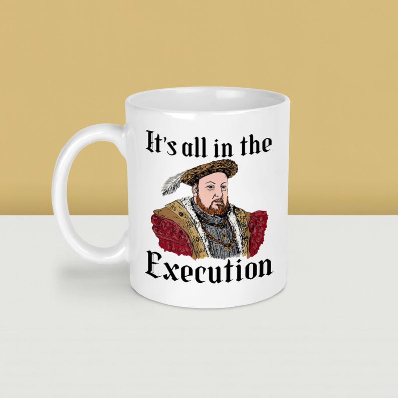 May include: White ceramic mug featuring a portrait of a historical figure with a feathered hat and ornate clothing. The mug has the text "It's all in the Execution" in black lettering.