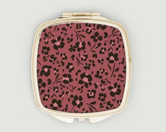 Espejo compacto con estampado floral de leopardo en rosa oscuro y negro.