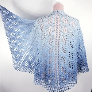 May include: A light blue crochet shawl with a delicate lace pattern. The shawl is made with a gradient yarn that transitions from a darker blue to a lighter blue.
