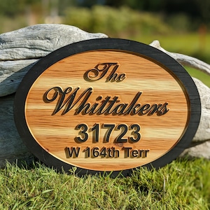 May include: A round wooden sign with a black border. The sign has the text "The Whittakers 31723 W 164th Terr" engraved on it.