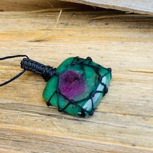 Könnte beinhalten: Ein grüner und rosafarbener Edelstein-Anhänger mit einer schwarzen Schnur. Der Edelstein ist mit schwarzem Garn umwickelt.