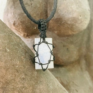 May include: A white crystal pendant with a black cord necklace. The crystal is encased in a black macrame star design.