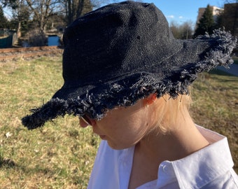 May include: A black bucket hat with a frayed brim. The hat is made of a woven fabric and has a casual, relaxed style.