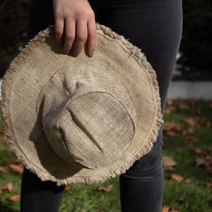 May include: A brown, wide-brimmed hat made of natural fibers with a frayed edge. The hat is held by a person's hand.