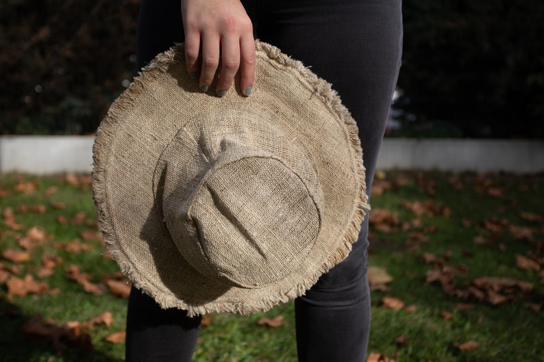May include: A brown, wide-brimmed hat made of natural fibers with a frayed edge. The hat is held by a person's hand.