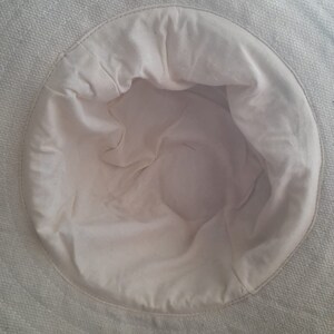 May include: The inside of a white canvas hat. The hat is made of a soft, woven fabric. The hat is unlined and has a smooth, white interior.