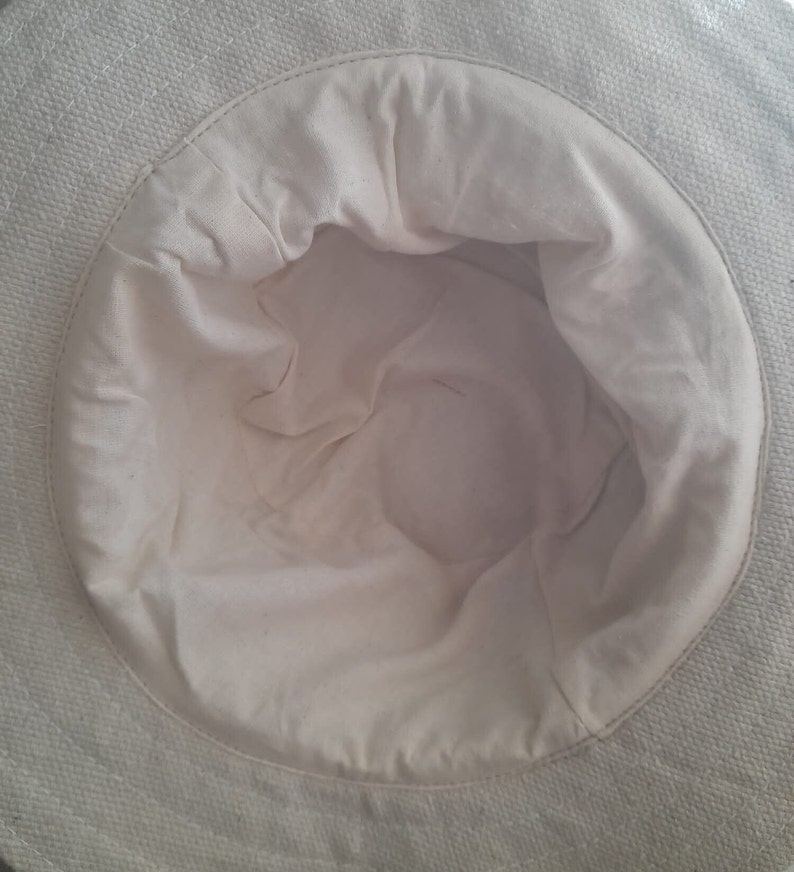 May include: The inside of a white canvas hat. The hat is made of a soft, woven fabric. The hat is unlined and has a smooth, white interior.