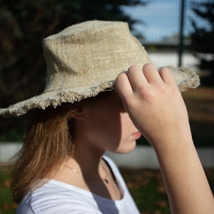 May include: A light brown, wide-brimmed hat with frayed edges. The hat is made of a natural material and has a casual, relaxed style.