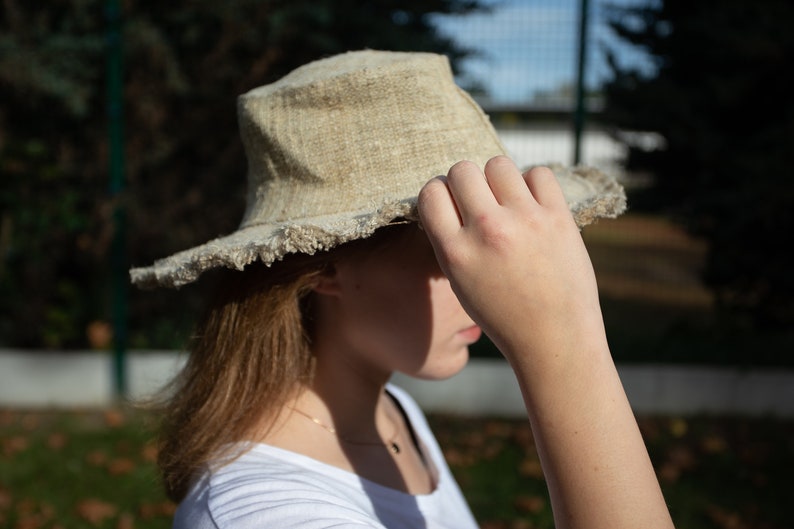 May include: A light brown, wide-brimmed hat with frayed edges. The hat is made of a natural material and has a casual, relaxed style.
