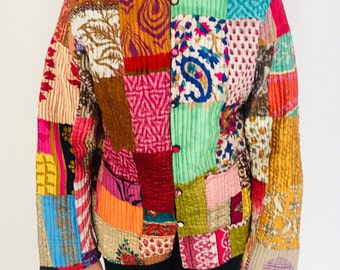 Op de afbeelding: Een kleurrijk patchwork gequilte jas met een knoopsluiting en lange mouwen. De jas is gemaakt van verschillende stoffen met verschillende patronen en kleuren, waaronder roze, rood, groen, blauw en geel.