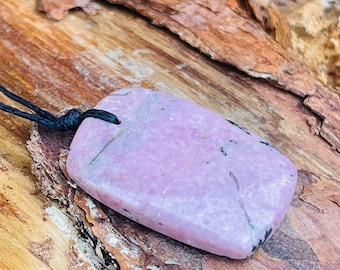 May include: A light pink and black stone pendant on a black cord. The stone has a smooth, polished surface and is shaped like a rectangle.