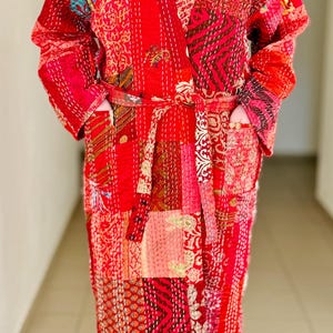 May include: A red quilted robe with a patchwork design and a tie belt. The robe has a floral pattern and is made of a soft, comfortable fabric.
