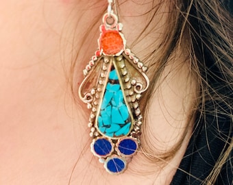 May include: Silver dangle earrings with turquoise and blue stones. The earrings have a teardrop shape with a silver filigree design.
