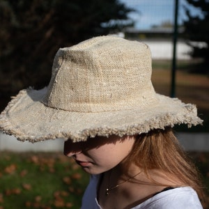 May include: A wide-brimmed hat made of natural fibers with a frayed edge. The hat is light brown and has a simple design.