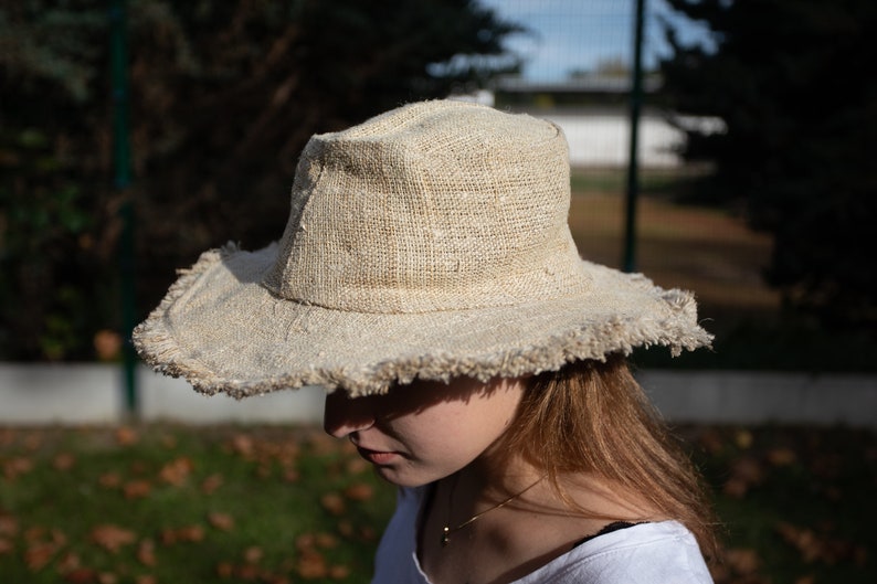 May include: A wide-brimmed hat made of natural fibers with a frayed edge. The hat is light brown and has a simple design.