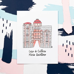 以下が含まれることがあります： 赤い屋根のピンクの建物の水彩画。建物には「Casa de Cultura Mario Quintana」と書かれています。イラストは青とピンクの筆致で囲まれています。