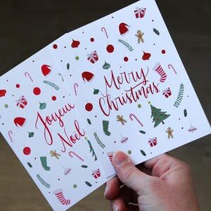 K&ouml;nnte beinhalten: Zwei Weihnachtskarten mit festlichen Designs. Eine Karte sagt "Joyeux Noel" und die andere sagt "Merry Christmas".