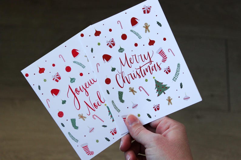 K&ouml;nnte beinhalten: Zwei Weihnachtskarten mit festlichen Designs. Eine Karte sagt "Joyeux Noel" und die andere sagt "Merry Christmas".