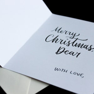 K&ouml;nnte beinhalten: Eine wei&szlig;e Karte mit schwarzer Kalligraphie, auf der "Frohe Weihnachten, Liebling" und "Mit Liebe," steht.