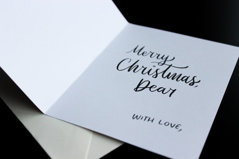 K&ouml;nnte beinhalten: Eine wei&szlig;e Karte mit schwarzer Kalligraphie, auf der "Frohe Weihnachten, Liebling" und "Mit Liebe," steht.