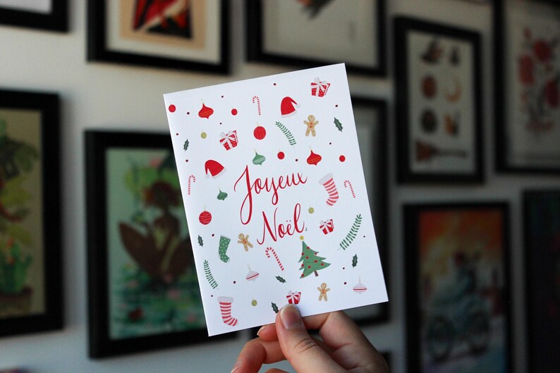 K&ouml;nnte beinhalten: Eine wei&szlig;e Karte mit einem roten und gr&uuml;nen Weihnachtsmotiv. Die Karte tr&auml;gt die Aufschrift "Joyeux No&euml;l" in roter Kursivschrift.