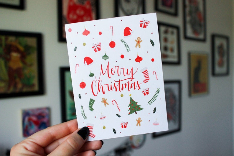K&ouml;nnte beinhalten: Eine wei&szlig;e Weihnachtskarte mit roten und gr&uuml;nen Illustrationen von Zuckerstangen, Kugeln, Str&uuml;mpfen, Lebkuchenm&auml;nnern und einem Weihnachtsbaum. Die Karte lautet "Frohe Weihnachten" in roter Kursivschrift.