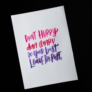 May include: A white card with a motivational quote written in pink and purple calligraphy. The quote reads "Don't hurry, don't worry, do your best, leave the rest."