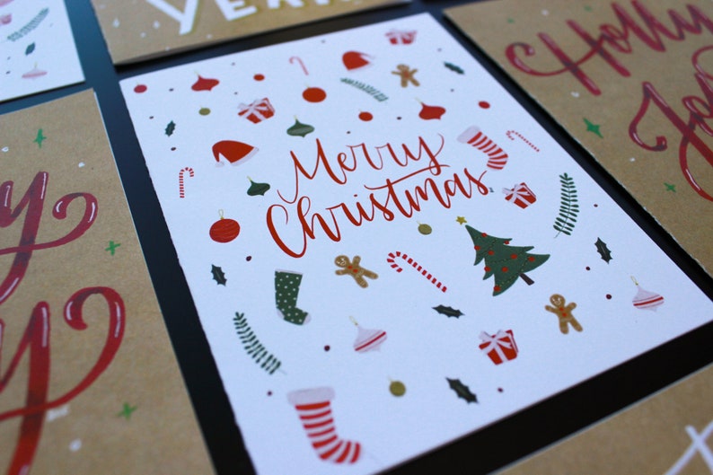 K&ouml;nnte beinhalten: Wei&szlig;e Karte mit roter Aufschrift "Merry Christmas". Die Karte ist mit roten und gr&uuml;nen Weihnachtsornamenten, Zuckerstangen und einem Weihnachtsbaum verziert.