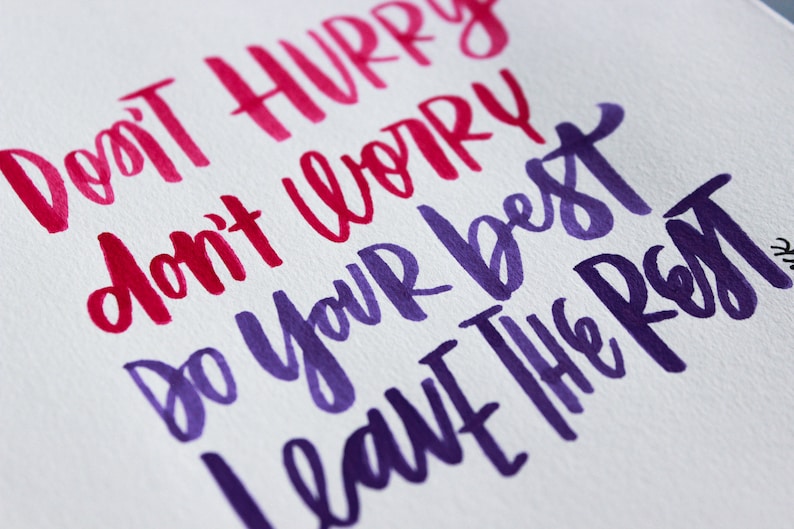 May include: Hand-lettered inspirational quote in pink and purple ink on white paper. The quote reads "Don't hurry, don't worry, do your best, leave the rest."