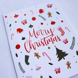 K&ouml;nnte beinhalten: Eine wei&szlig;e Weihnachtskarte mit einer roten "Frohe Weihnachten"-Botschaft, umgeben von festlichen Illustrationen von Ornamenten, Zuckerstangen, Lebkuchenm&auml;nnern, Str&uuml;mpfen und einem Weihnachtsbaum.