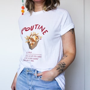 May include: White t-shirt with a red graphic of a poutine dish. The graphic includes the word "Poutine" and a definition: "Fries with gravy and cheese curds that are dark savory, yummy in a bowl."