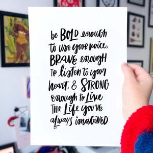 May include: Black and white inspirational quote handwritten on a white card. The quote reads: "be BOLD enough to use your voice, BRAVE enough To listen to your heart, & STRONG enough to live The Life you've always imagined"