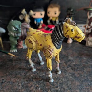 Könnte beinhalten: Ein gelbes Spielzeugpferd mit einem Used-Look, das braune, rostähnliche Flecken aufweist. Das Pferd hat eine schwarze Mähne und einen schwarzen Schweif, und seine Beine sind eine Kombination aus Gelb und Silber. Ein einzigartiges Sammlerstück im Vintage-Stil.