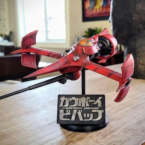 Puede incluir: Un modelo rojo y negro de la nave espacial "Swordfish II" de la serie de anime "Cowboy Bebop". El modelo está sobre una base negra con una placa plateada que dice "Cowboy Bebop" en japonés e inglés.