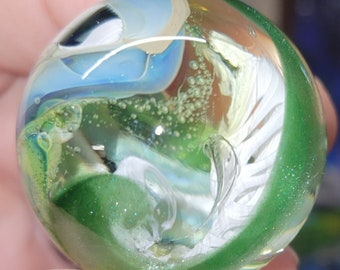 May include: A green, white, and blue glass marble with a swirling pattern and small air bubbles trapped inside.