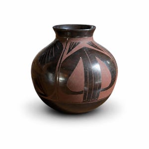 May include: A round, dark brown ceramic vase with a wide body and a narrow neck. The vase features a reddish-brown central design with black linear patterns. The design includes leaf-like shapes and vertical lines. The vase is likely handmade and has a glossy finish.